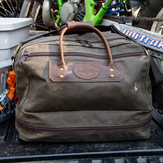 Frost River's waxed canvas and leather Prairie Boot Bag sitting in the back of a pickup truck with a dirt bike.