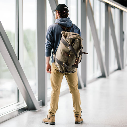 A man wearing the Explorer Duffel ESB which is a waxed canvas duffle bag equipped with back straps.