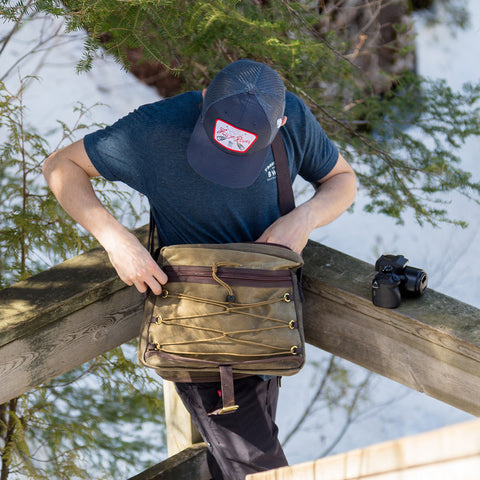 A man grabbing a camera out of a waxed canvas messenger bag.