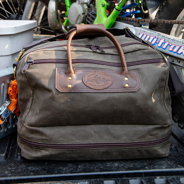 Frost River's waxed canvas and leather Prairie Boot Bag sitting in the back of a pickup truck with a dirt bike.  