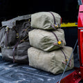 Three sizes of waxed canvas travel organizer bags stacked up and sitting on a tailgate at a campsite. 