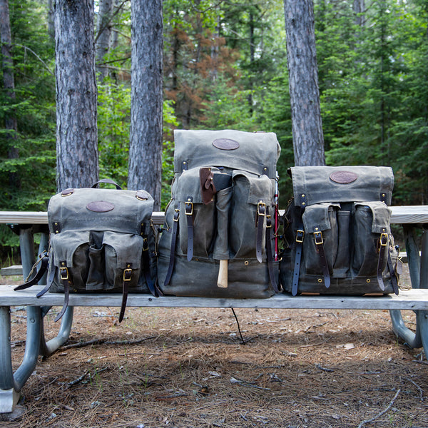 Frost River's three different sized Isle Royale Bushcraft Packs sitting next to each other on a campsite bench. 
