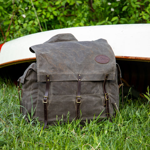 A traditional waxed canvas canoe pack sitting in front of a canoe after a portage. 
