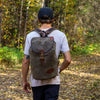 A man wearing a traditionally styled waxed canvas rucksack backpack. 