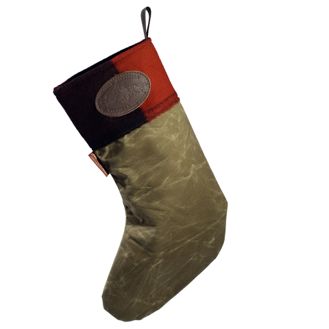 A Christmas stocking with a textured olive green body, a red and patchwork cuff, and a brown leather logo patch on the side.
