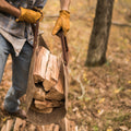 A man working outside carrying firewood with a waxed canvas log carrier.