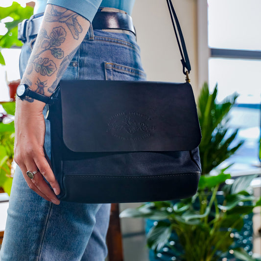 A woman carrying a shoulder bag made from black waxed canvas and leather.