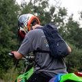 A black waxed canvas daypack on the back of a man riding a dirt bike.