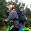A black waxed canvas daypack on the back of a man riding a dirt bike.