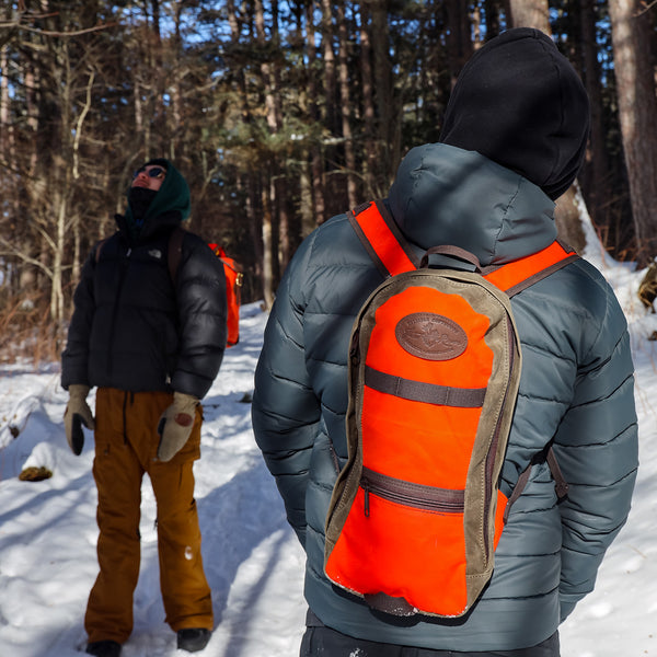 A man wearing the hunter orange two tone version of the waxed canvas High Falls Short-Day Pack.